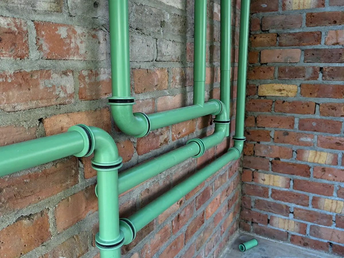 New green PPR water pipes with elbow and tee fittings installed along a brick wall