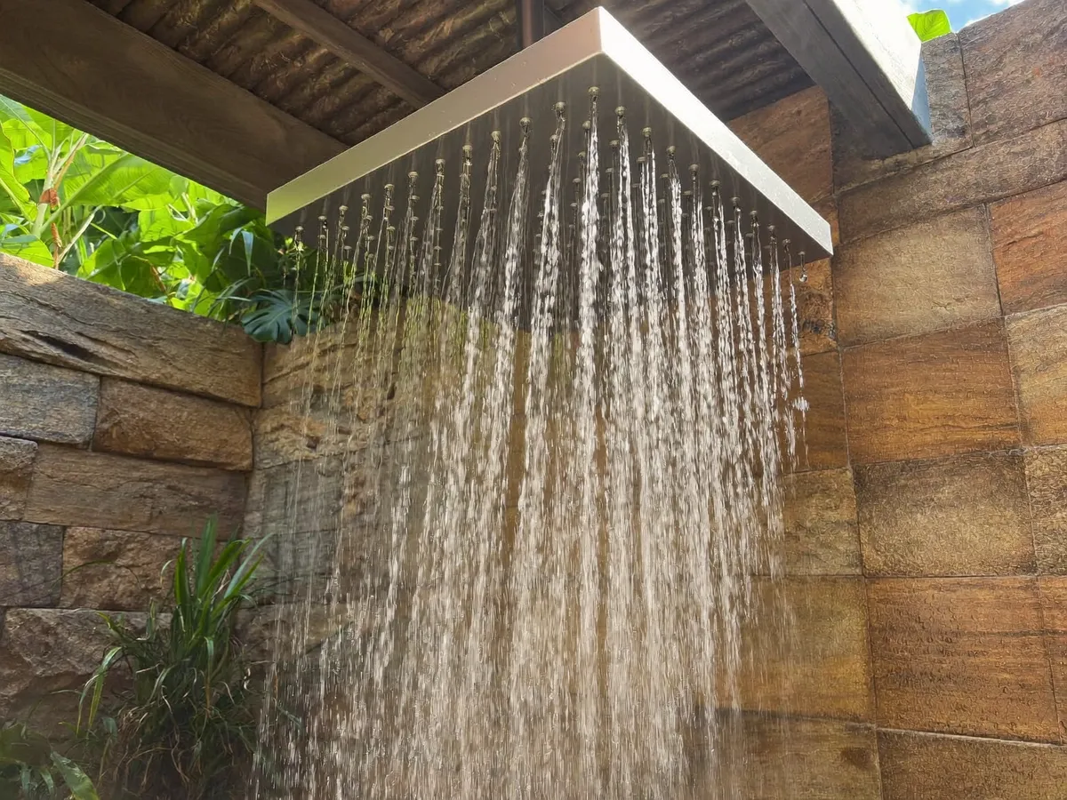 Rain shower head streaming water in an open-air Bali stone shower